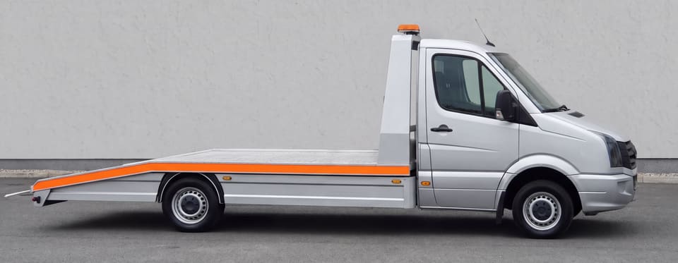 Srebrni šlep iz profila: visoka kabina, prazna aluminijumska platforma sa narandžastom trakom i narandžasta svetlosna rampa na uzglavlju.